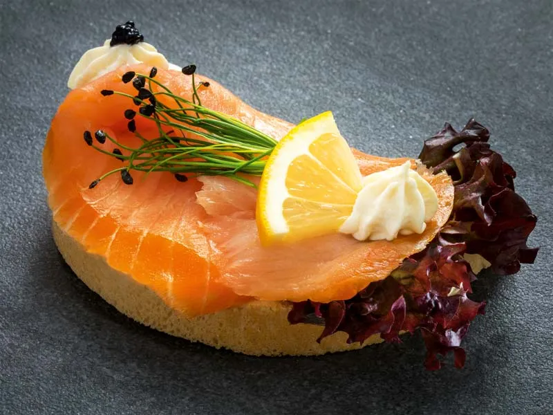 Ein einzelnes Brötchen reichlich belegt mit frischem Räucherlachs.