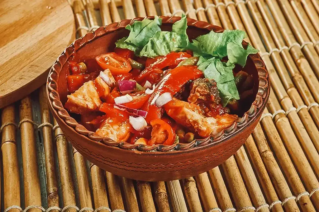 Ein farbenfroher Đuveč, bosnischer Gemüseeintopf mit Huhn, in einem traditionellen Tontopf serviert.