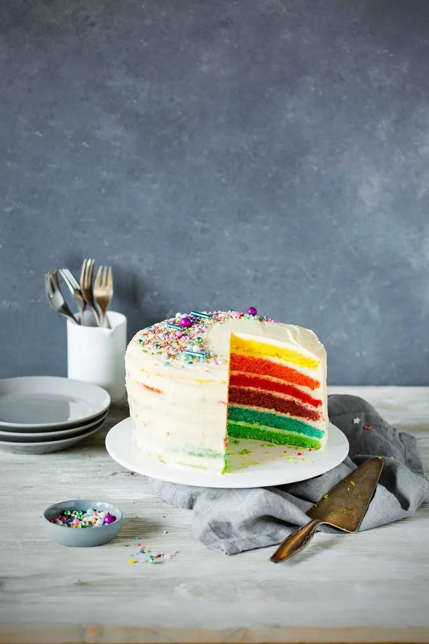 Ein farbenfroher Regenbogenkuchen mit Schichten und cremigem Cheesecake-Frosting, ideal für Kinderfeste