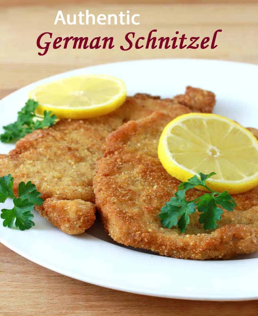 Ein fertig gebratenes Schweineschnitzel, goldbraun und knusprig, auf einem Teller mit Zitrone und Petersilie