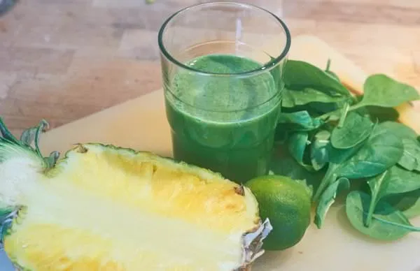 Ein frisch zubereiteter Ananas-, Limetten- und Spinatsaft in einem Glas, garniert mit Minze und Limettenscheiben.