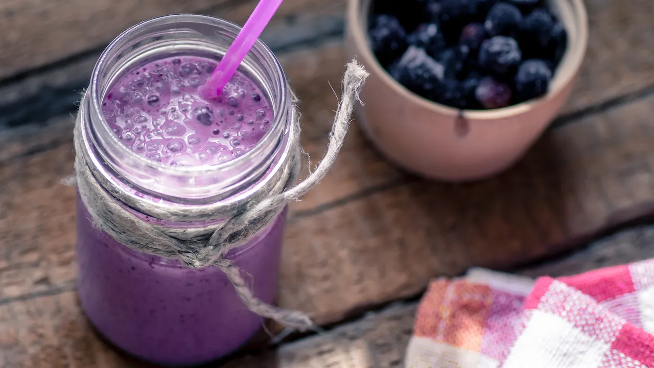 Ein Frozen Berry Joghurt-Smoothie in einem Glas, garniert mit frischen Beeren und Minze, auf einem Holztisch