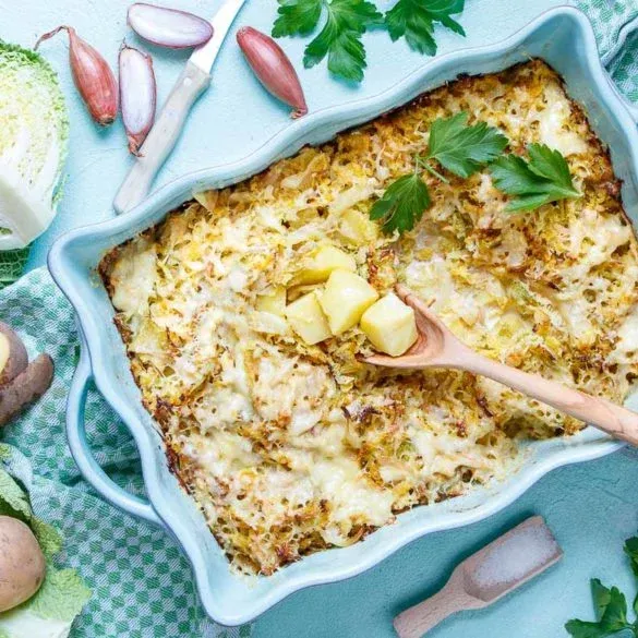 Ein ganzer Wirsingkohl auf einem Schneidebrett, daneben einige geschnittene Wirsingblätter und Kartoffelwürfel