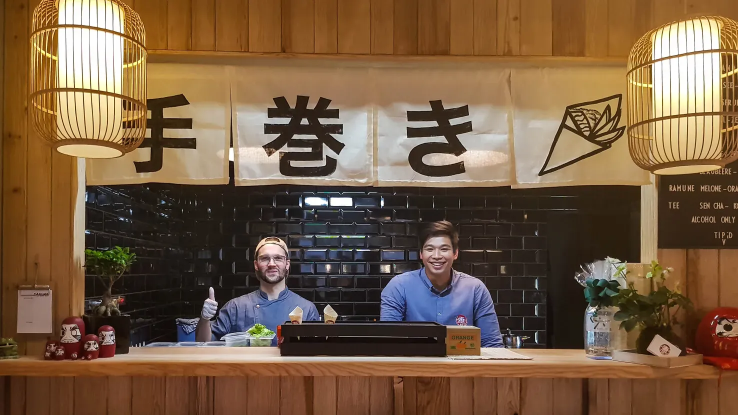 Ein gemütliches, hell eingerichtetes Sushi-Lokal mit modernen Holzmöbeln und Schaukeln als Sitzgelegenheiten, japanische Dekorationen an den Wänden.