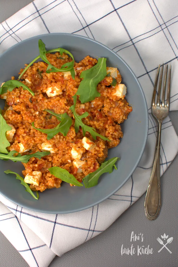 Ein Gericht Tomaten-Perlgraupen-Risotto mit Feta und Rucola, angerichtet auf einem Teller
