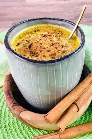 Ein Glas Goldene Milch, garniert mit Zimt und einem Sternanis, auf einem dunklen Holztisch