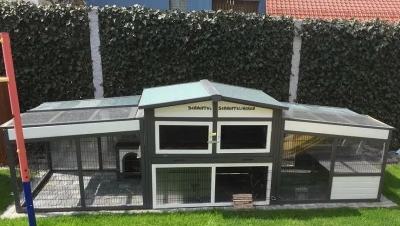 Ein großes Außengehege für Kaninchen im Garten, umgeben von Grün