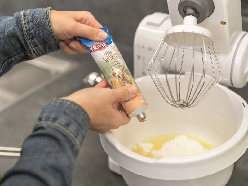 Ein Hundeleckerli-Teig wird sorgfältig in die Mulden einer blauen Silikon-Backmatte gestrichen