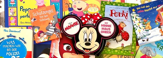 Ein Kind blättert fasziniert in einem bunten Bilderbuch, während ein Erwachsener daneben sitzt und vorliest.