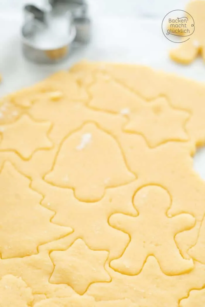 Ein Kind hilft beim Ausrollen des Mürbeteigs und Ausstechen von Plätzchen mit weihnachtlichen Formen