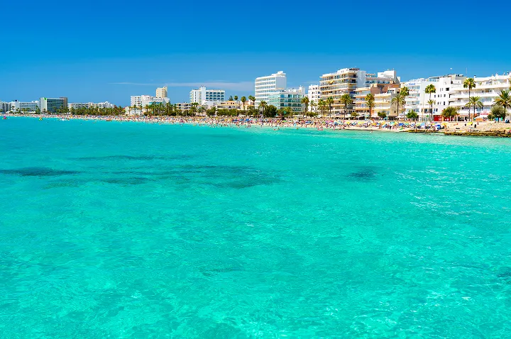 Ein klarer blauer Ozean erstreckt sich bis zum Horizont unter einem strahlend blauen Himmel bei Cala Millor, Mallorca.
