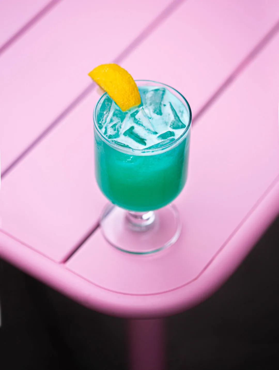 Ein leuchtend türkiser Cocktail in einem eleganten Glas, garniert mit einer Zitronenscheibe, der unbeschwerten Genuss verspricht