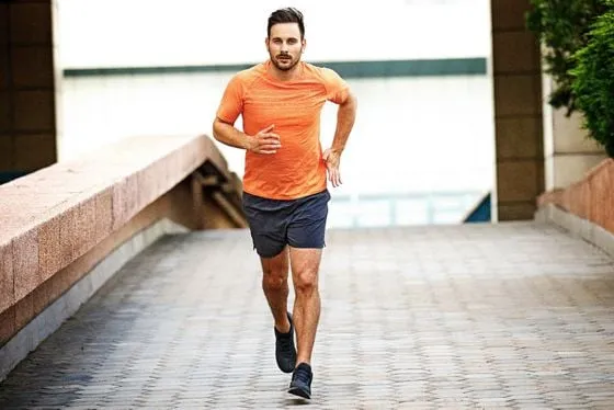 Ein Mann läuft auf einem gepflasterten Weg in einer städtischen Umgebung. Er trägt ein orange T-Shirt und dunkle Shorts.