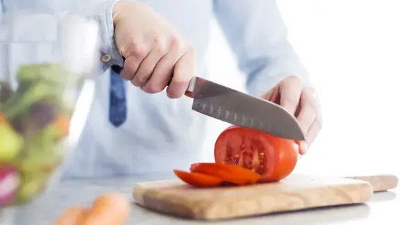 Ein Mann schneidet eine Tomate auf einem Holzbrett in Scheiben.