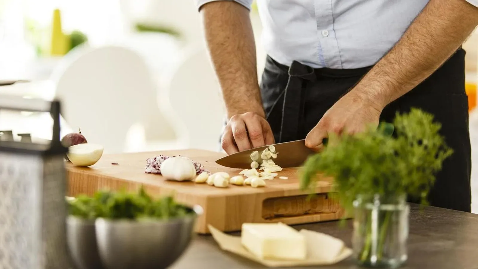 Ein Mann schneidet Knoblauchzehen auf einem Holzbrett für die Zubereitung