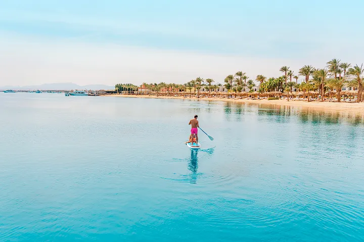 Ein Mann steht auf einem Paddleboard und gleitet über das ruhige Wasser des Roten Meeres in Ägypten.