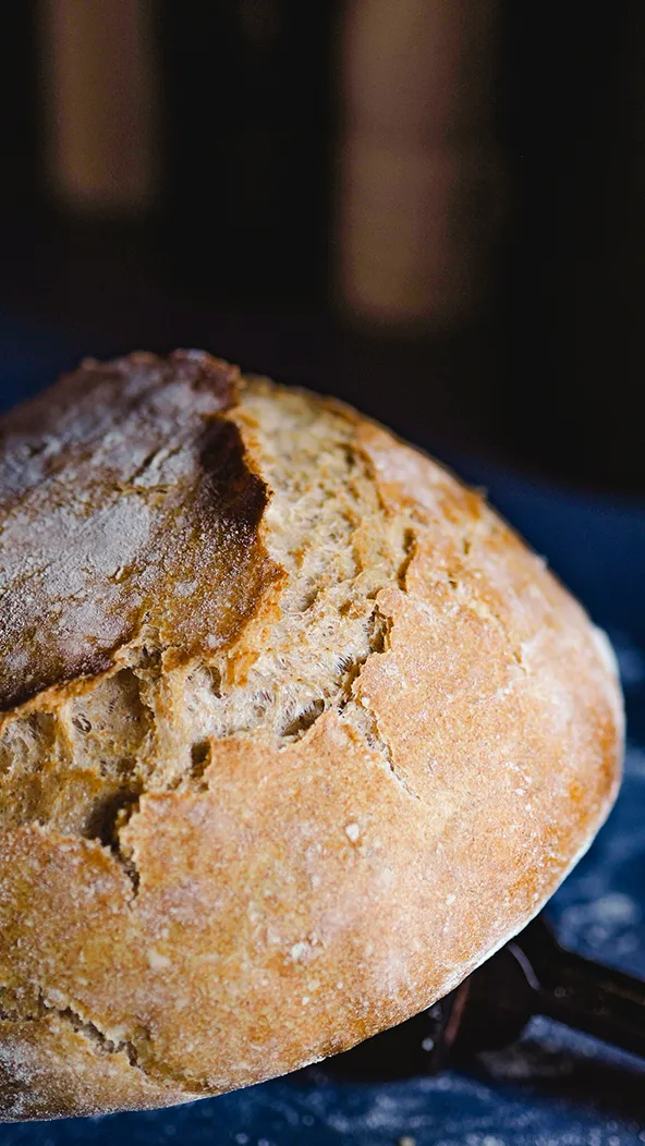 Ein perfekt gebackenes Brot mit knuspriger Kruste, das aus einem Gusseisentopf gehoben wird