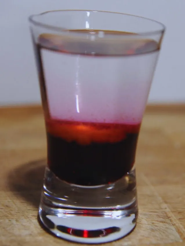 Ein polnischer Wściekły Pies (Mad Dog) Shot mit Himbeersirup, Wodka und Tabasco, geschichtet in einem Glas.