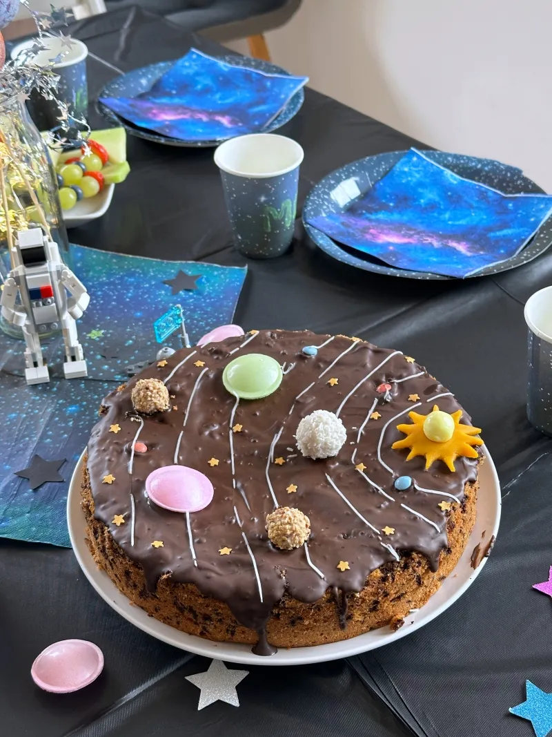 Ein runder Kuchen, der als Planetensystem mit verschiedenen Süßigkeiten und Zuckerschrift dekoriert ist.