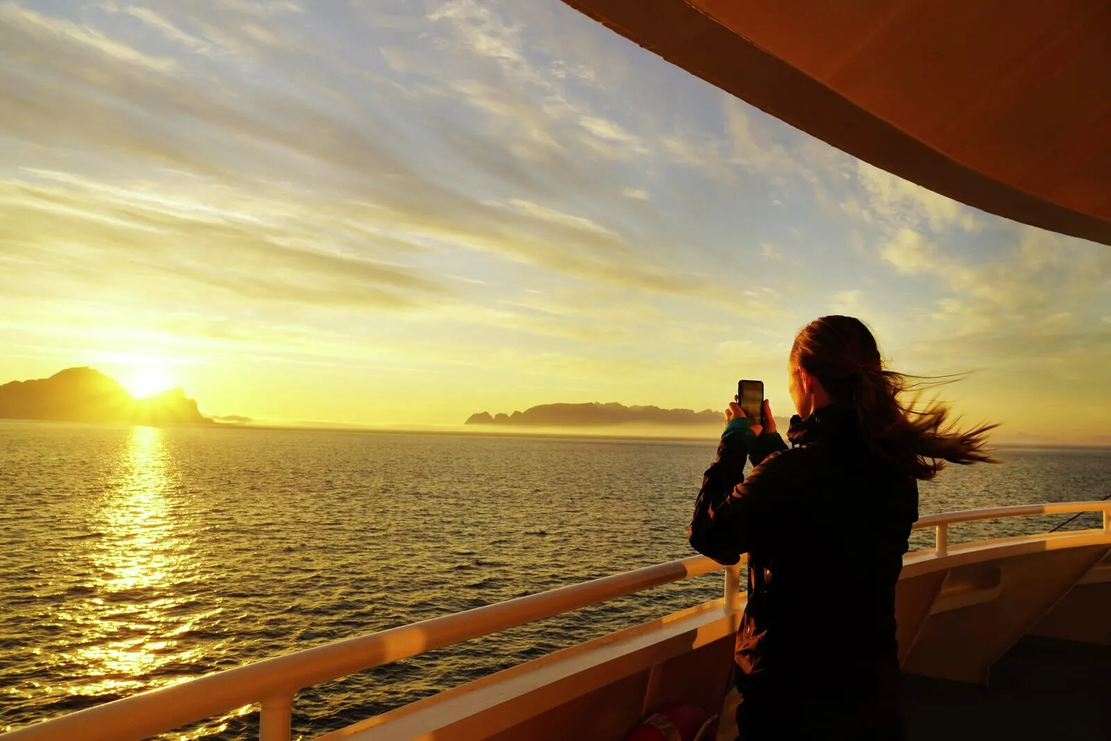 Ein Schiff unter der Mitternachtssonne auf dem Meer, umgeben von dramatischen Wolken