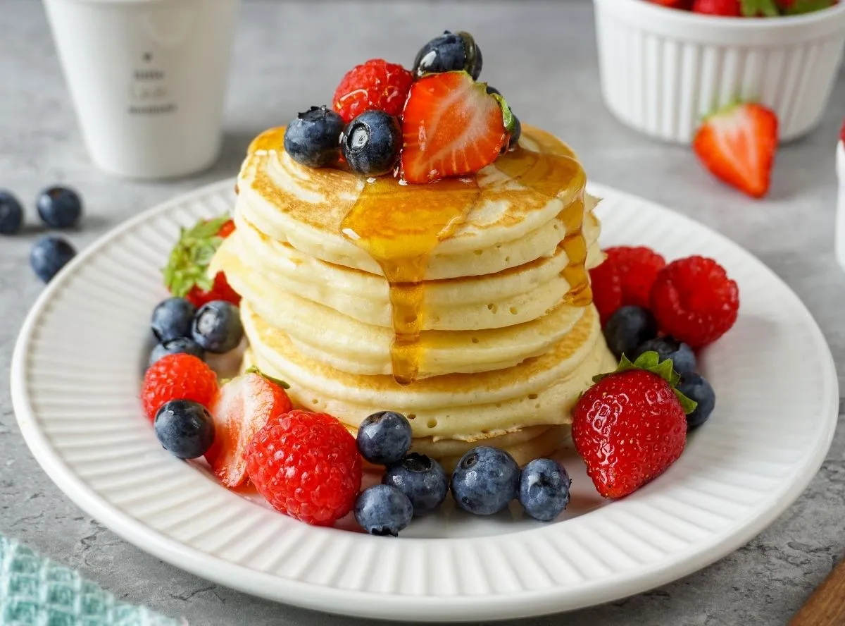 Ein Stapel goldbrauner Pancakes, übergossen mit Sirup und frischen Beeren, auf einem Teller
