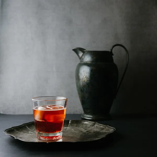 Ein stimmungsvoller roter Cocktail mit einem grauen Krug im Hintergrund, der eine elegante Atmosphäre schafft