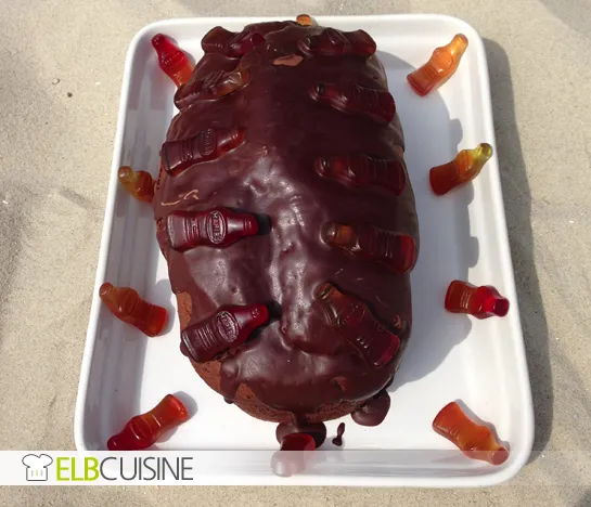 Ein Stück kultiger Cola-Kuchen mit Schokoladenguss und Gummibärchen-Colaflaschen auf einem Teller