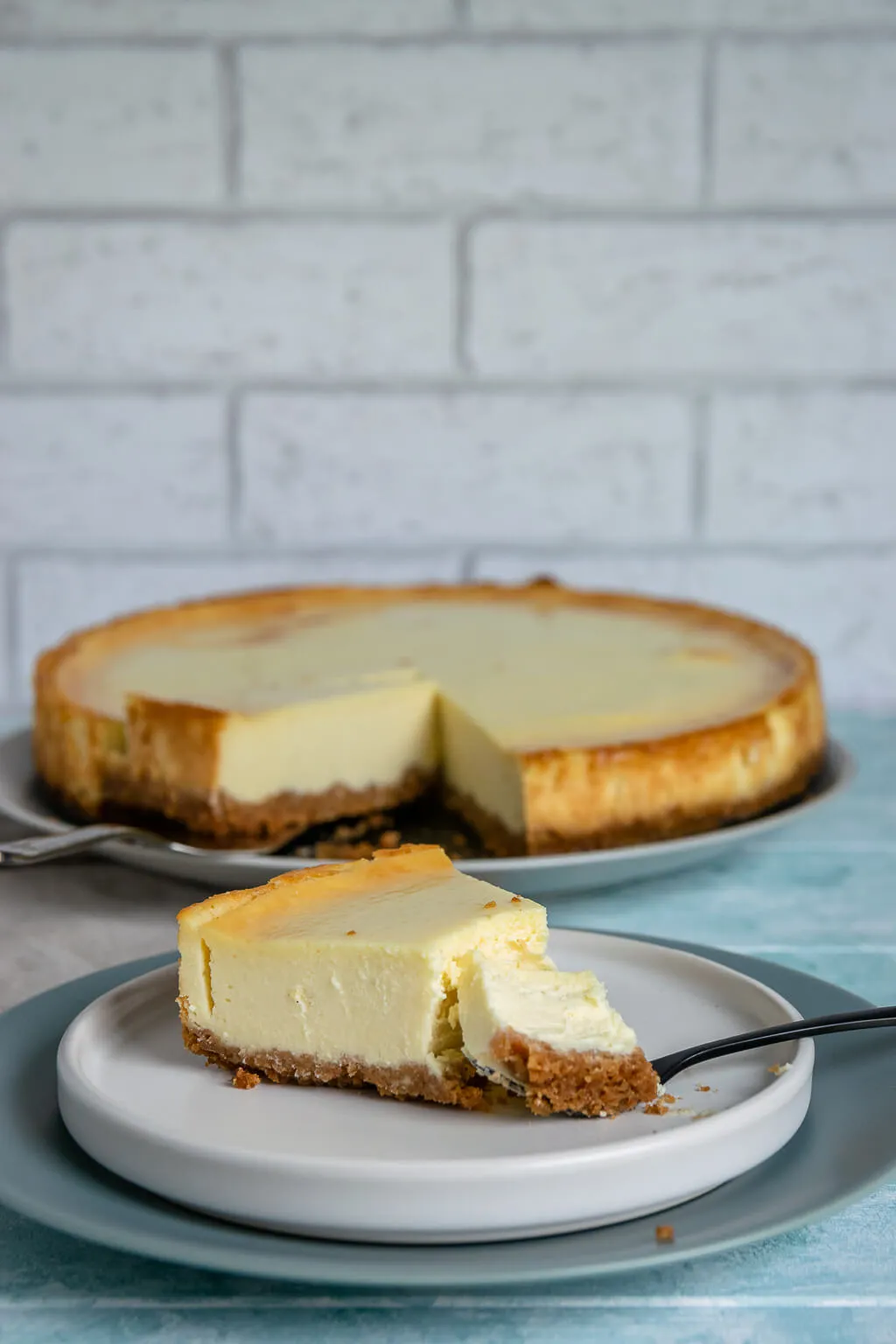 Ein Stück New York Cheesecake auf einem Teller, perfekt gebacken mit einer leicht goldenen Oberfläche, daneben eine Gabel