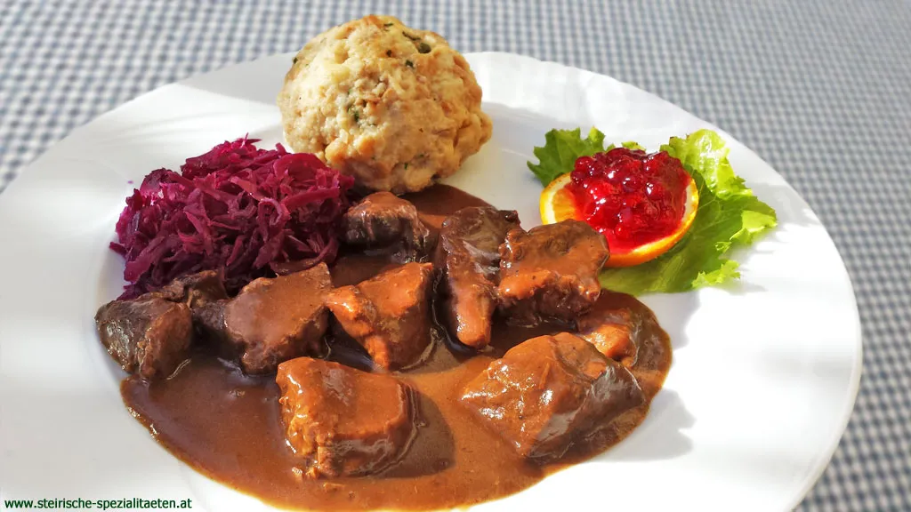 Ein Teller Hirschgulasch, kunstvoll angerichtet mit Rotkraut und Knödeln, verziert mit einem Lorbeerblatt