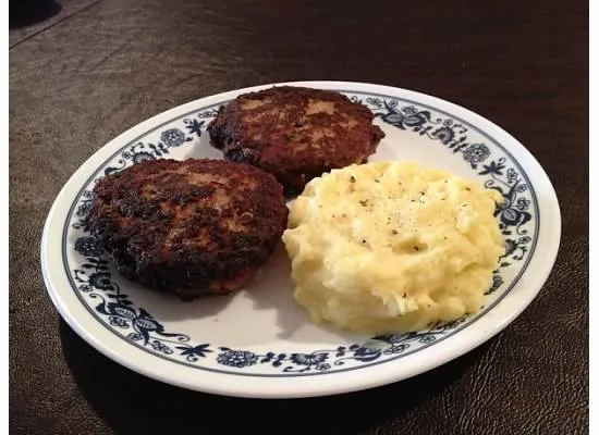 Ein Teller mit frisch gebratenen Faschierten Laibchen, serviert mit cremigem Erdäpfelpüree und frischer Petersilie