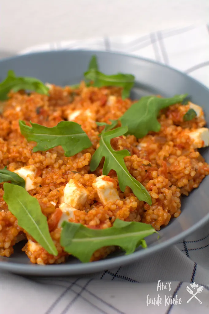 Ein Teller Tomaten-Graupen-Risotto, garniert mit frischem Rucola und Feta-Stückchen