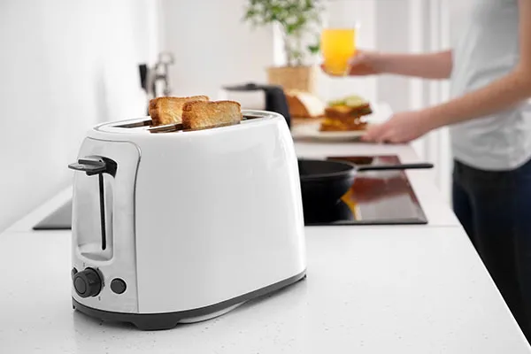 Ein Toaster auf einer Küchenzeile mit zwei Toastscheiben darin, im Hintergrund ein Mann