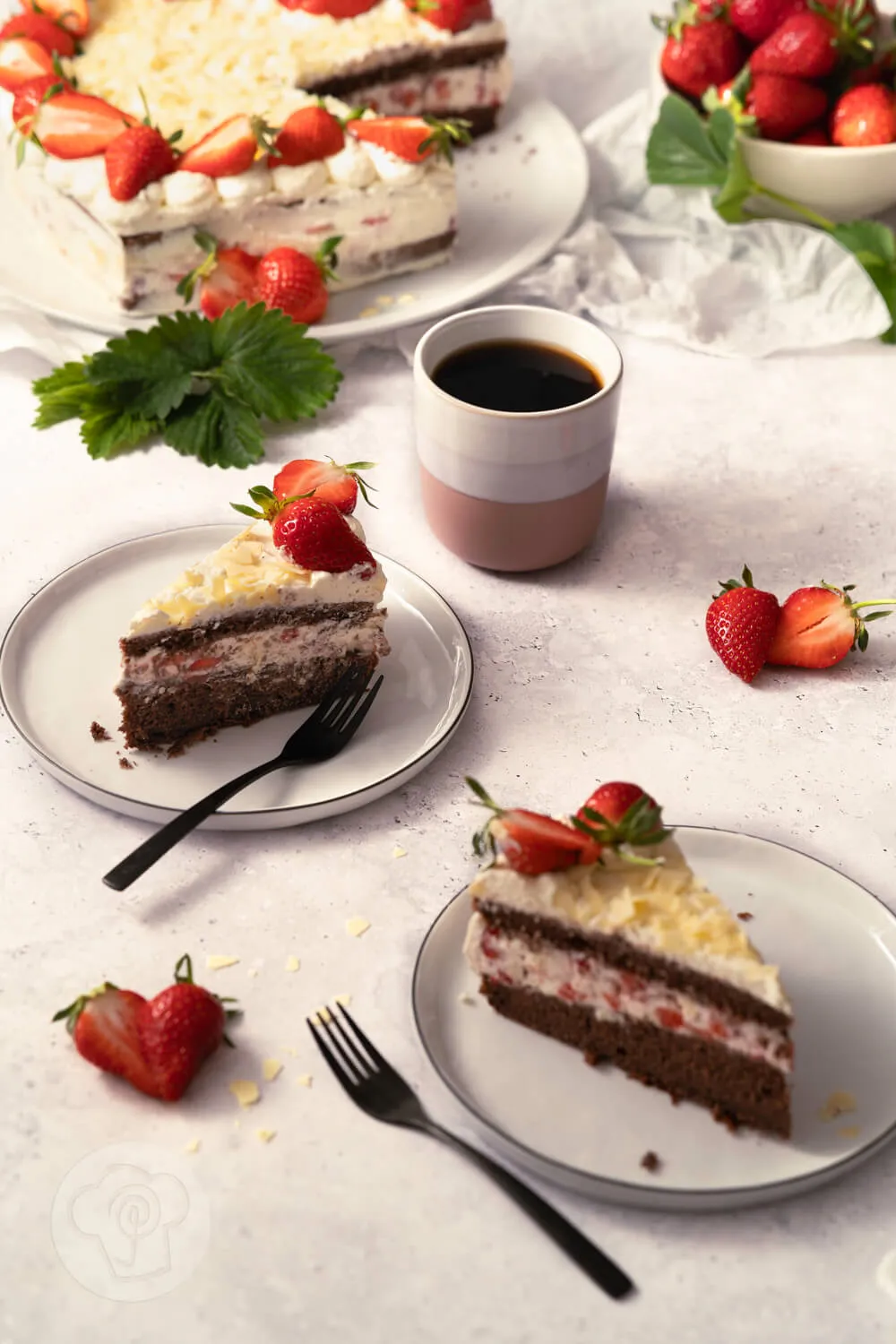 Eine angebissene Erdbeer Sahne Torte auf einem Teller, garniert mit Erdbeeren und Minzblättchen