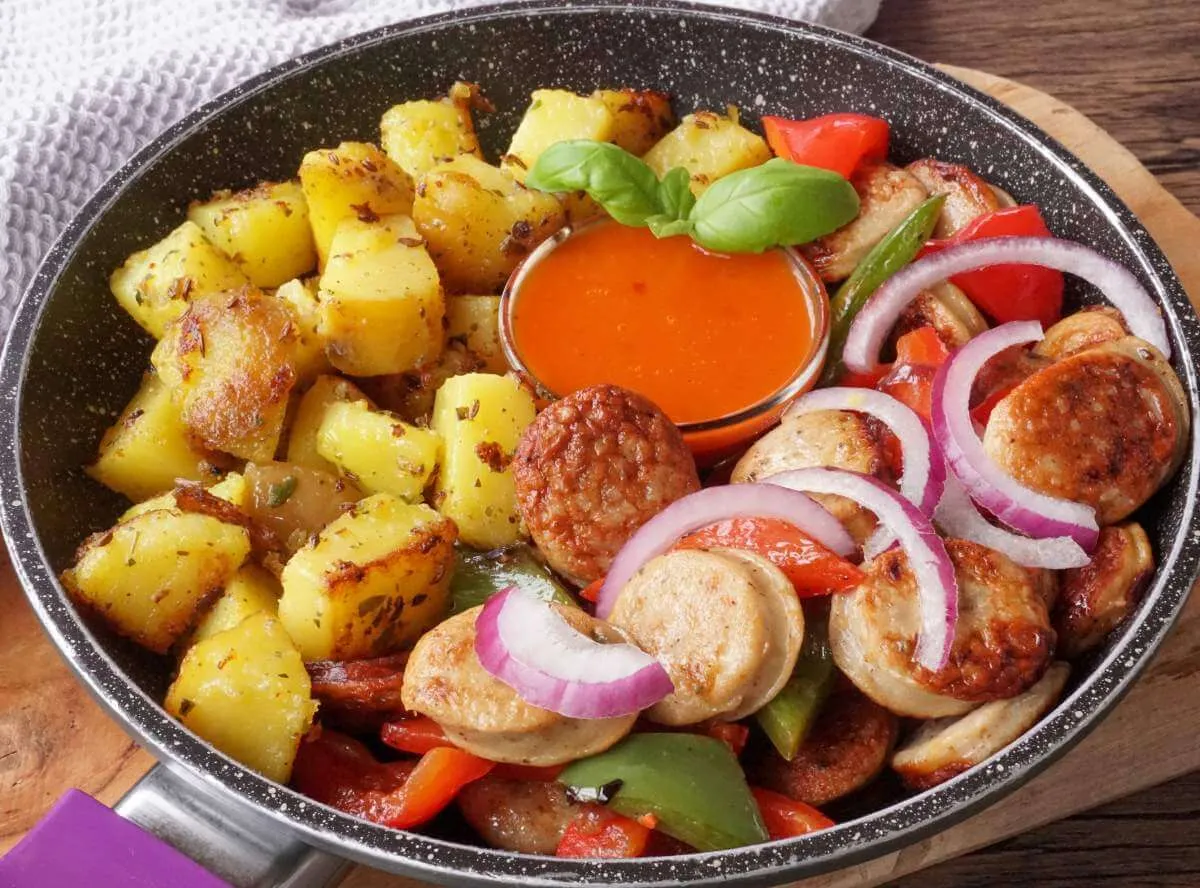 Eine bunte Bratwurstpfanne mit verschiedenen Gemüsesorten in einer gusseisernen Pfanne auf dem Herd
