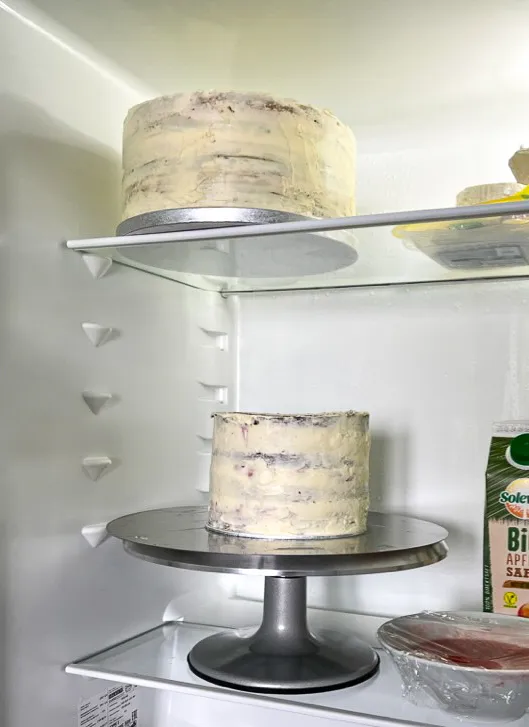 Eine detaillierte Ansicht des Schichtens einer mehrstöckigen Torte, mit Cremes, Fruchteinlagen und Böden, bereit für die Kühlung.