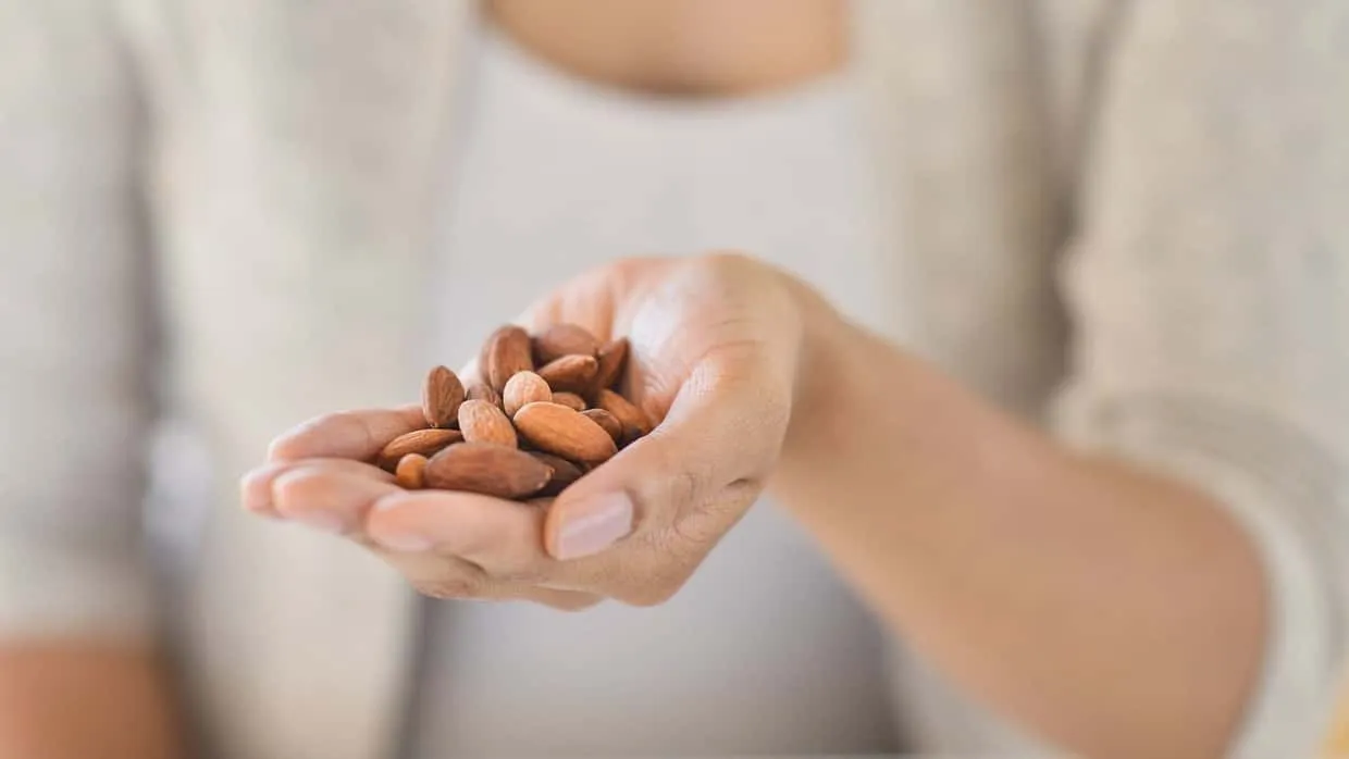 Eine Frau hält eine Handvoll Mandeln als gesunden und energiereichen Snack für zwischendurch.