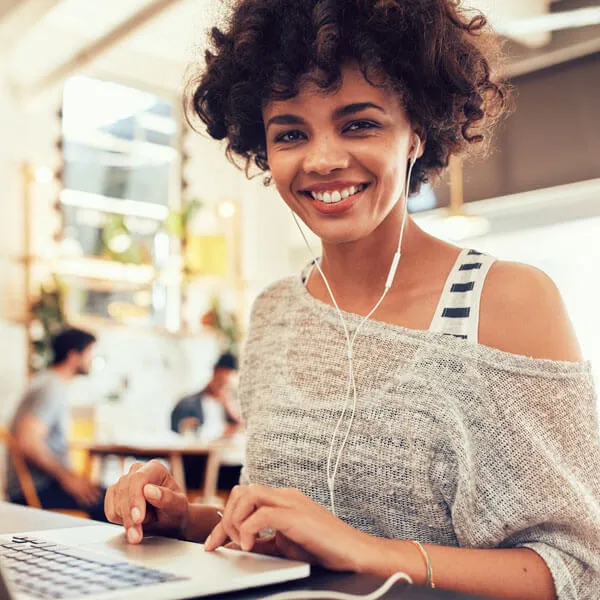 Eine Frau mit In-Ear-Kopfhörern sitzt vor einem Laptop und nimmt an einer Online-Weiterbildung teil, was Flexibilität und moderne Lernmethoden darstellt.