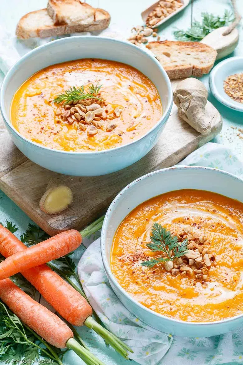 Eine große Kelle Möhrensuppe wird aus einem Topf in eine Schüssel gefüllt, bereit zum Servieren
