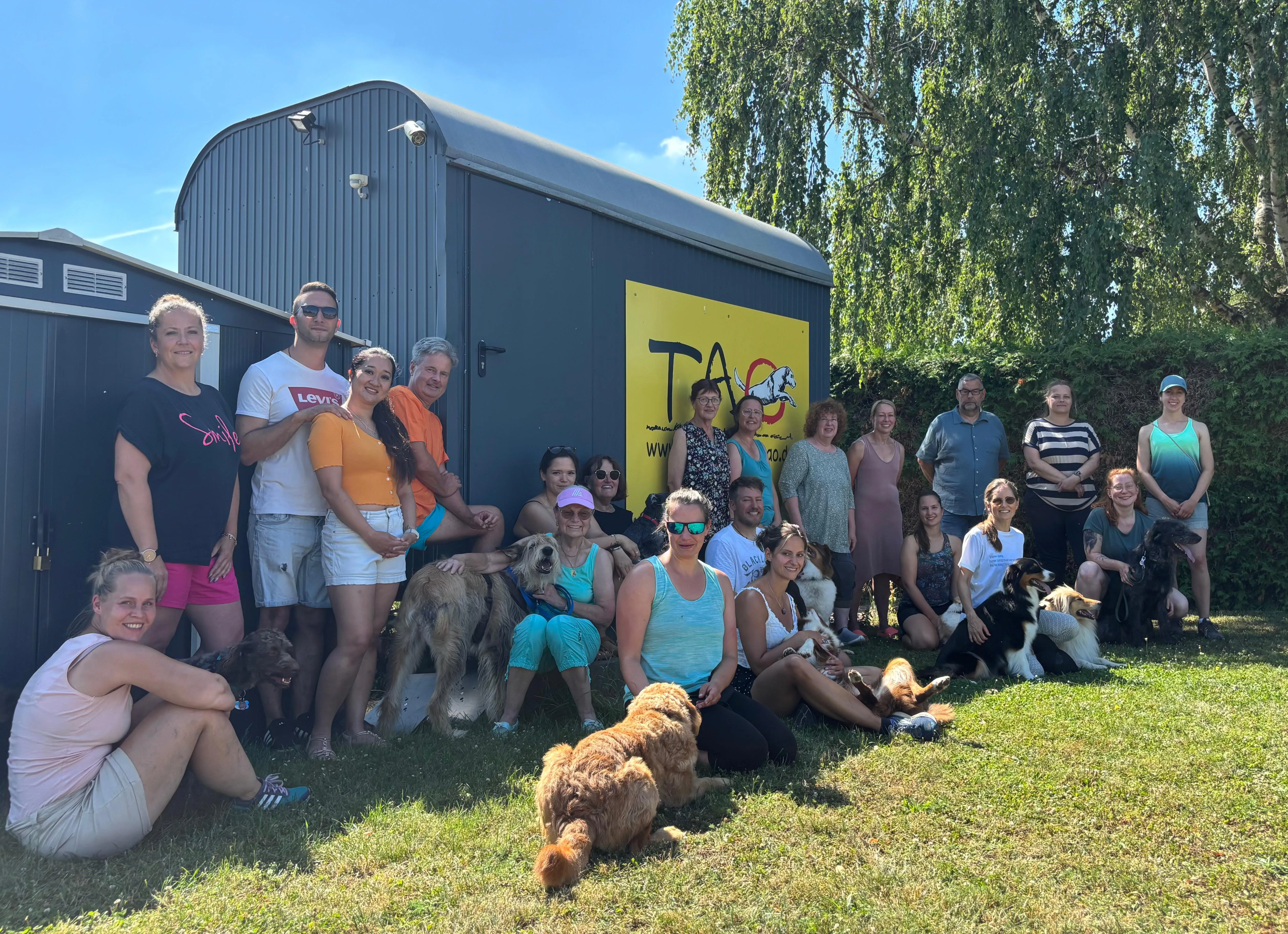 Eine Gruppe von Hundeführern mit ihren Hunden posiert nach der Begleithundeprüfung zusammen mit Prüfern und Helfern.