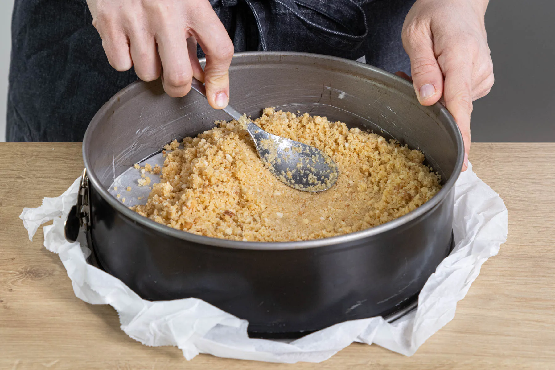 Eine Hand drückt die Keks-Butter-Masse fest in eine Springform