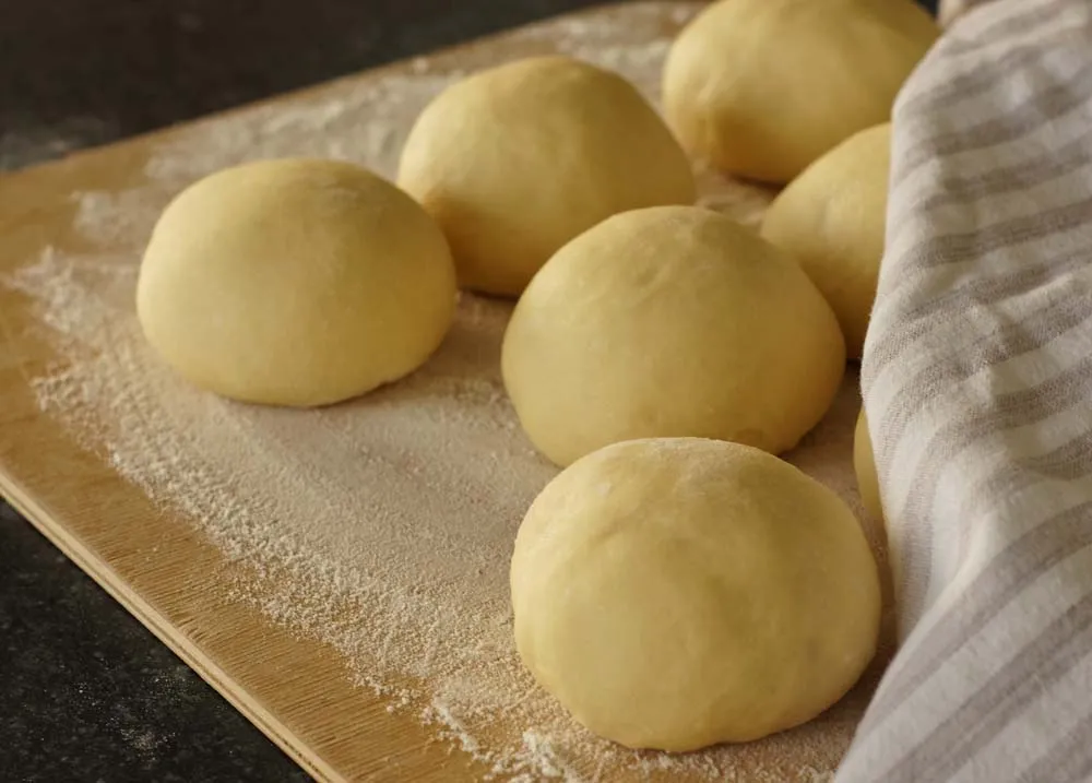 Eine Hand formt einen Hefekloß aus dem vorbereiteten Teig auf einer leicht bemehlten Fläche