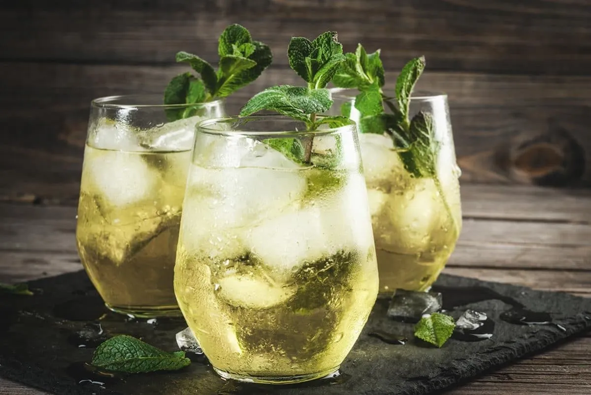 Eine Hand gießt Rebujito in ein Glas, das mit Eis und Minze gefüllt ist