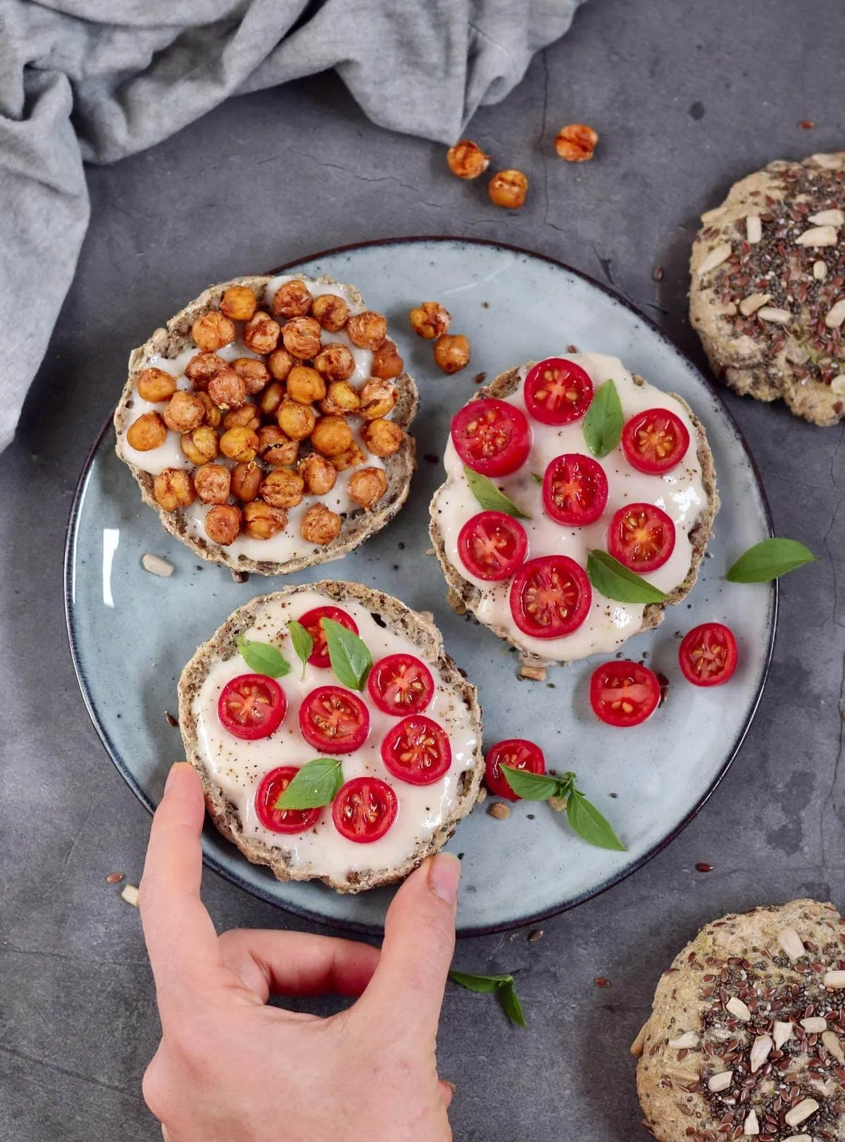 Eine Hand greift nach einem selbstgebackenen Brötchen, das mit Tomaten und veganem Mozzarella belegt ist