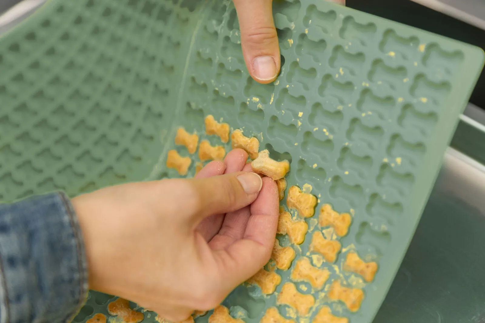 Eine Hand löst frisch gebackene Hundekekse in Knochenform von einer blauen Silikon-Backmatte ab