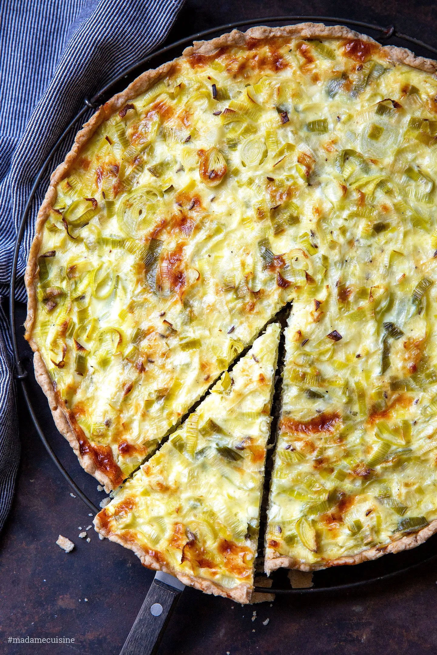 Eine Hand rollt Mürbeteig auf einer bemehlten Arbeitsfläche für eine Quiche aus