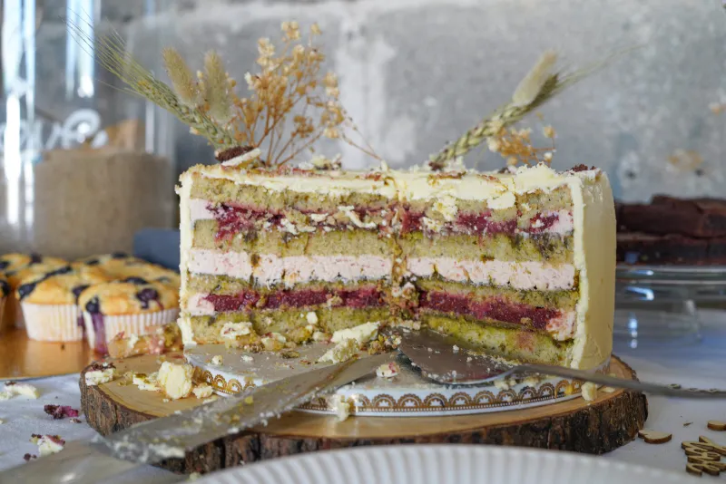 Eine Hochzeitstorte mit Pistazienböden, Pistazienmus, Erdbeercreme, Erdbeer-Himbeer-Fruchteinlagen und weißer Ganache, bereit für den Anschnitt und den Genuss.