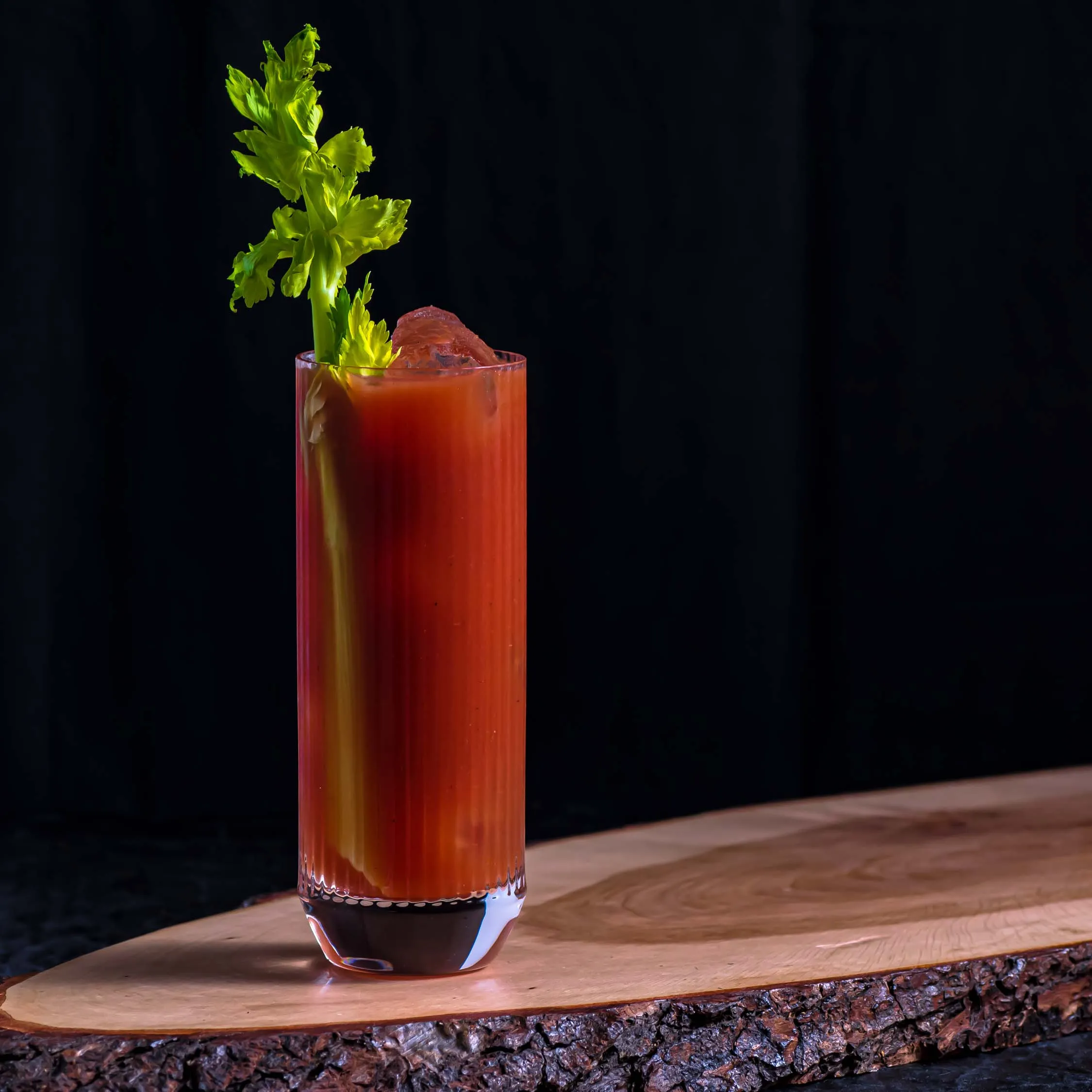 Eine klassische Bloody Mary, appetitlich garniert mit einer Selleriestange und Limettenspalte, serviert in einem hohen Glas auf einem dunklen Hintergrund.