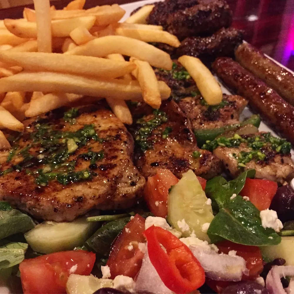 Eine köstliche Auswahl an gegrilltem Fleisch, Sudzuka Wurst und Cevapi mit Pommes und griechischem Salat, typisch für ein Balkan-Restaurant.