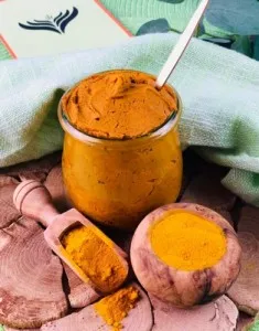 Eine Kurkuma-Power-Paste in einem Glas, umgeben von frischem Kurkuma und Gewürzen, symbolisiert die konzentrierte Anwendung