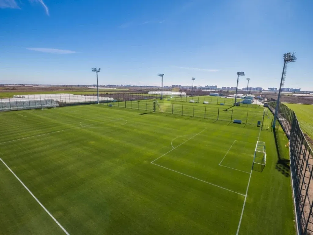 Eine moderne Fußballanlage mit mehreren Spielfeldern, umgeben von gepflegten Grünflächen und Gebäuden.
